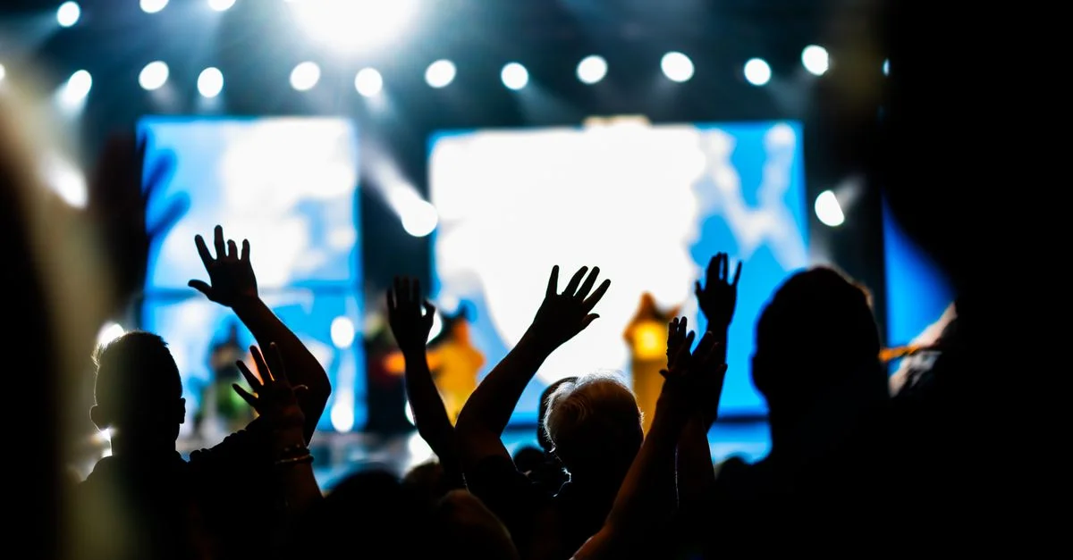 Silhouettes d'un public les mains levées lors d'un concert animé, illuminé par des projecteurs éclatants.