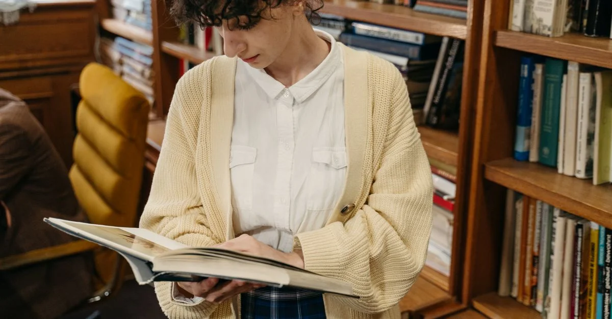 Une jeune femme en pull jaune lisant un livre dans un environnement de bibliothèque confortable.