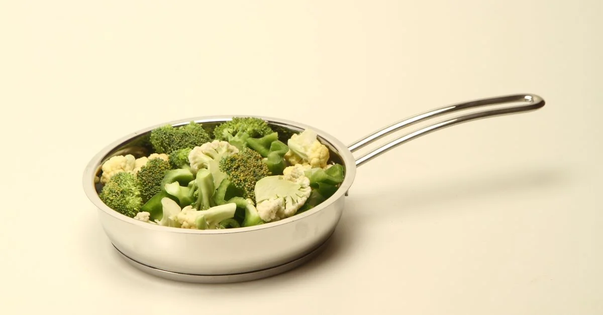 Bouquets de brocoli et de chou-fleur sains dans une poêle en acier inoxydable sur un fond uni.