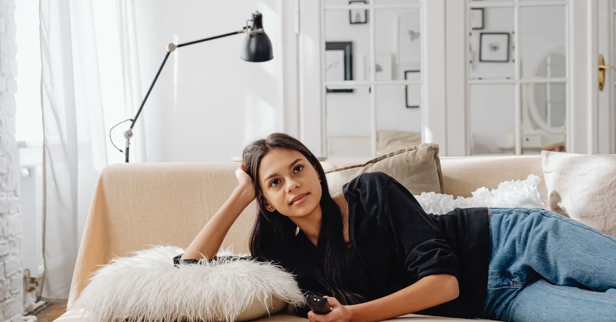 Femme se détendant confortablement sur un canapé avec une télécommande, profitant de son temps libre à l'intérieur.