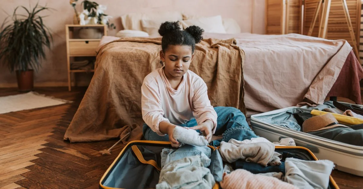 Une jeune fille pliant des vêtements dans une valise dans une chambre cozy avec une décoration naturelle.