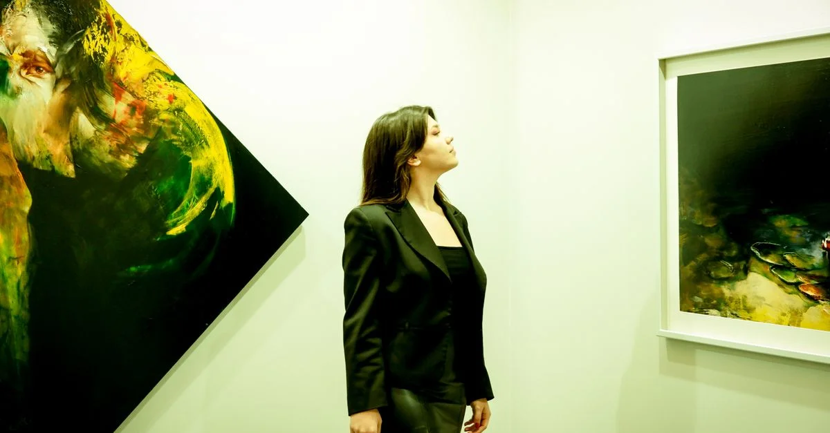 Une femme en tenue noire admirant des peintures abstraites dans une galerie d'art moderne.