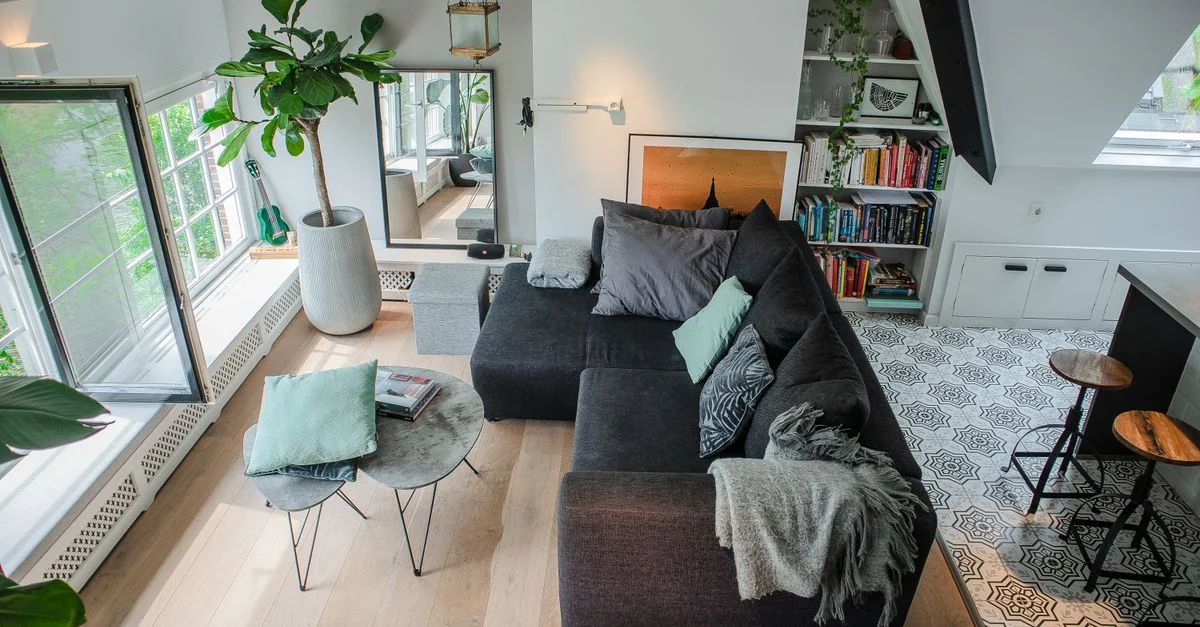 Salon moderne lumineux et élégant avec un grand canapé, des plantes et une lumière naturelle.